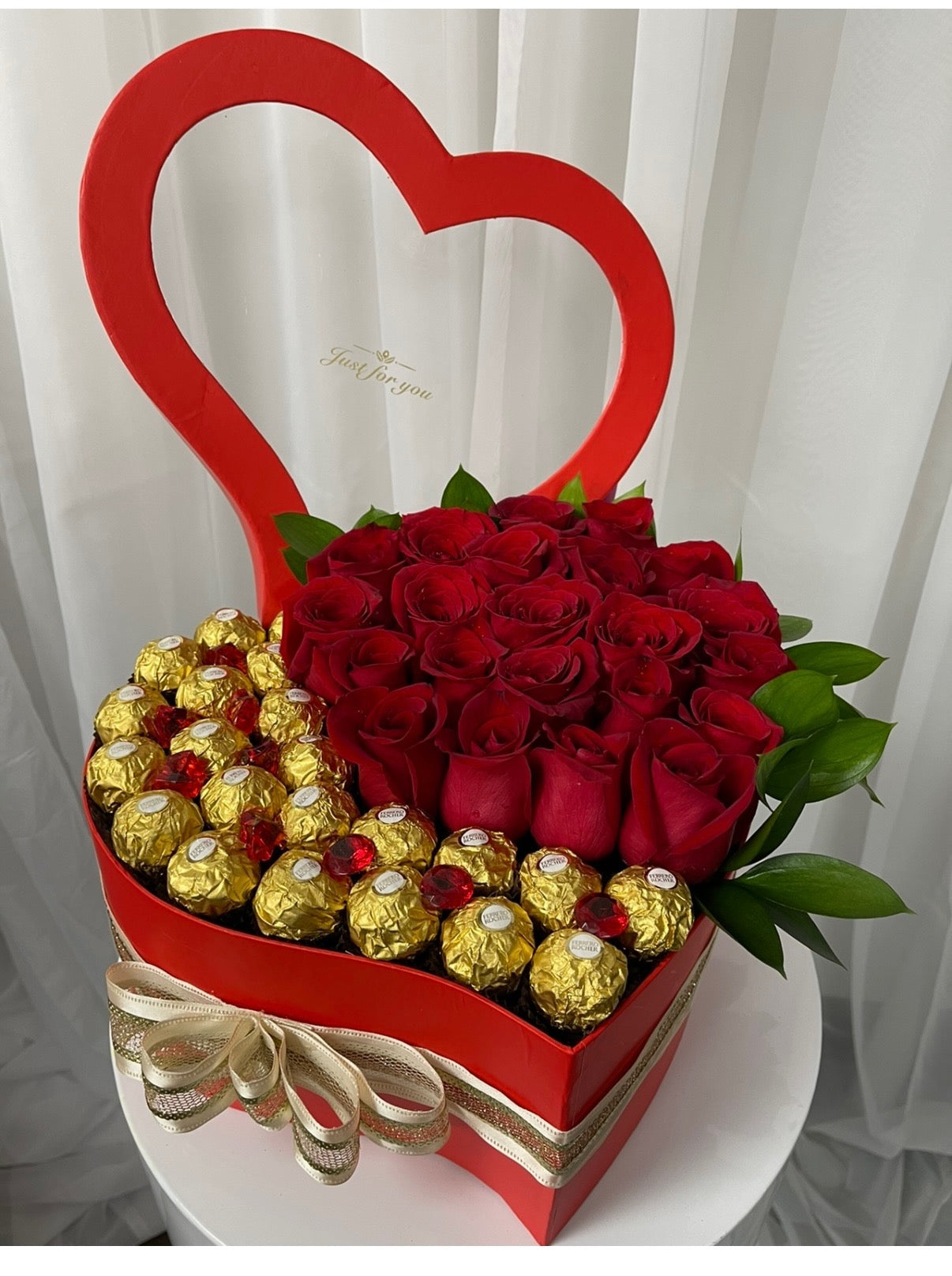 Heart-shaped box with red roses and gold chocolate candies on a white background