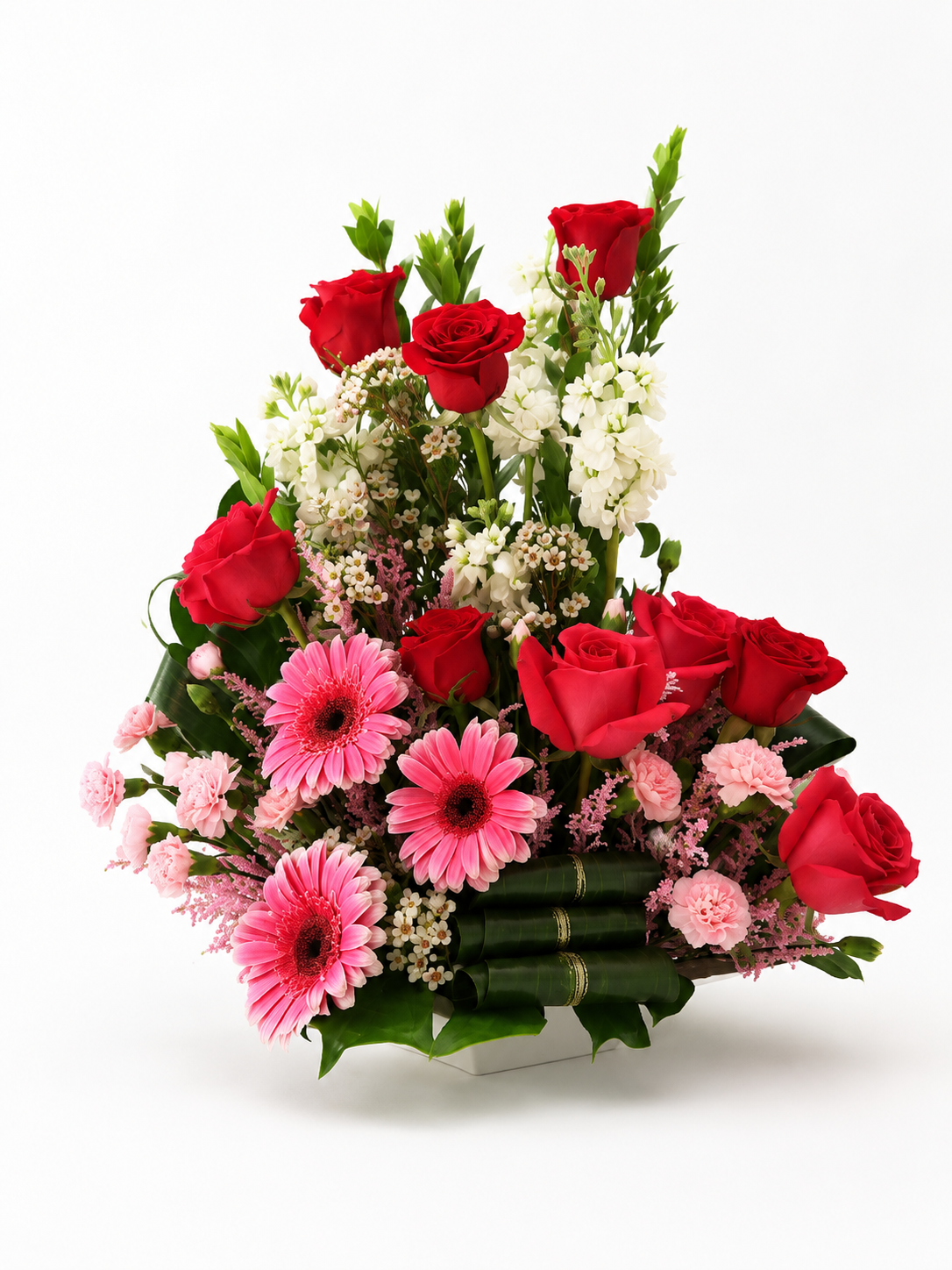 Bouquet of red roses and pink gerbera daisies in a decorative basket on a white background