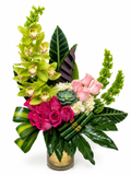 Floral arrangement with green orchids, pink roses, and succulents in a glass vase on a white background