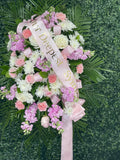 Floral arrangement with pink and white flowers and a 'Deepest Sympathy' ribbon on a green background.